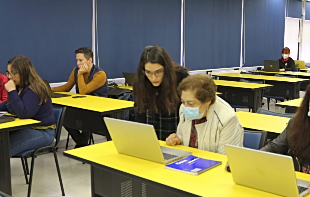 Bibliotecóloga explica a asistente de taller que está sentada mientras observa un computador.