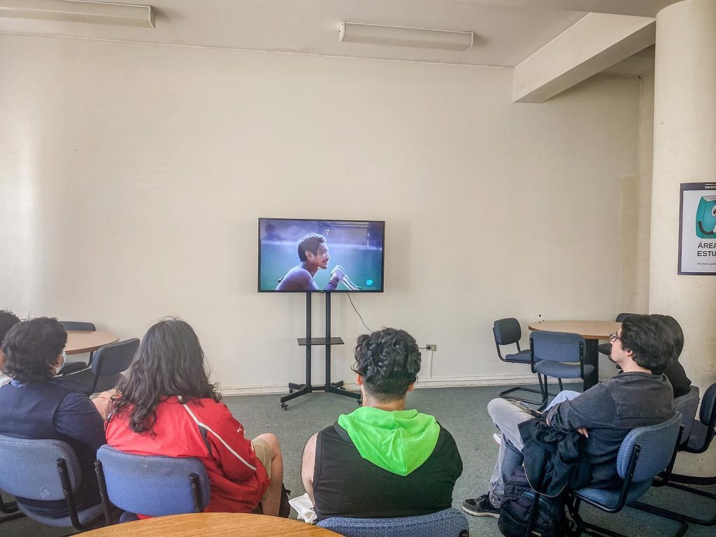 Estudiantes sentados en sillas negran miran una pantalla en espacio B de la Biblioteca de Ciencias Físicas y Matemáticas UdeC, durante ciclo de cine.