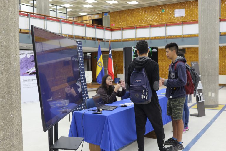 Estudiantes conversan con una de las encargadas del stand informativo instalado en el Hall de la Biblioteca Central UdeC.