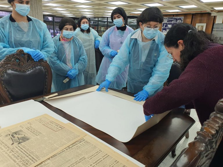 Equipo de Bibliotecas UdeC observa proceso de limpieza de diarios mientras es realizado por la conservadora Norka Carreño