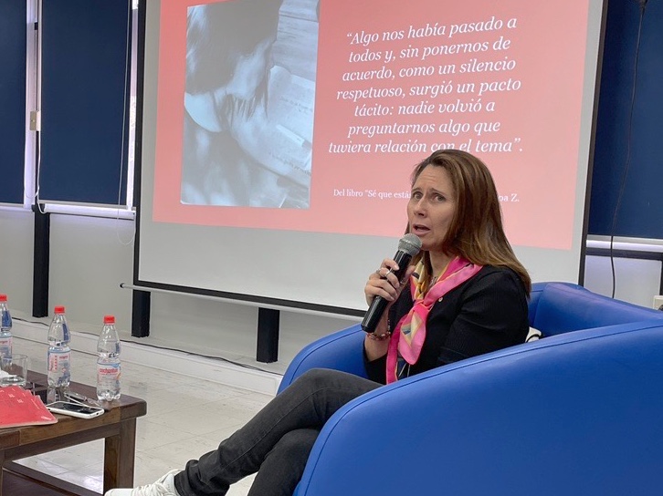Actriz Ana Luz Figueroa conversa con asistentes a presentación de su libro mientras está sentada en un sillón azul y sostiene un micrófono