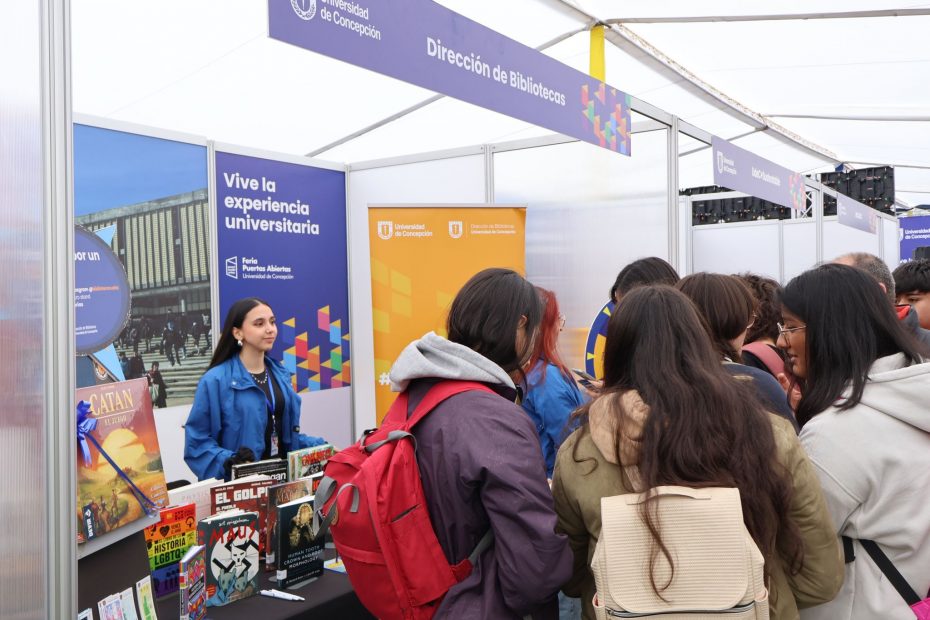 Estudiantes observan folletos informativos en stand de Bibliotecas UdeC ubicado en carpa de Feria Puertas Abiertas