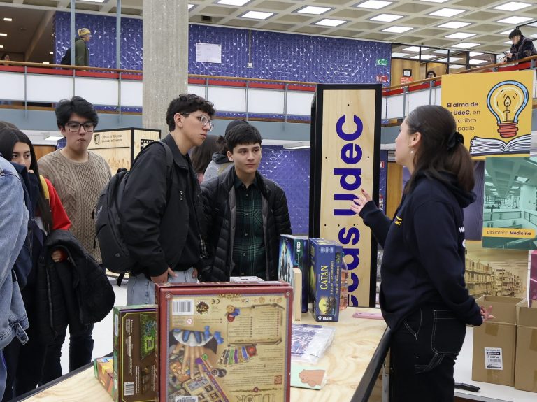 imagen que muestra a monitora conversando con asistentes a feria en hall de Biblioteca Central