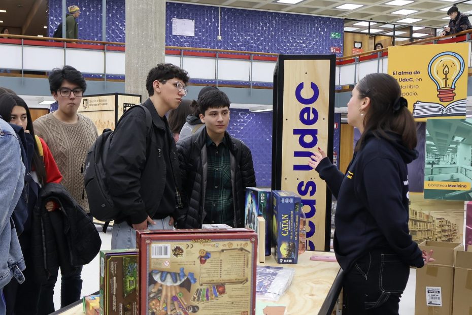 imagen que muestra a monitora conversando con asistentes a feria en hall de Biblioteca Central