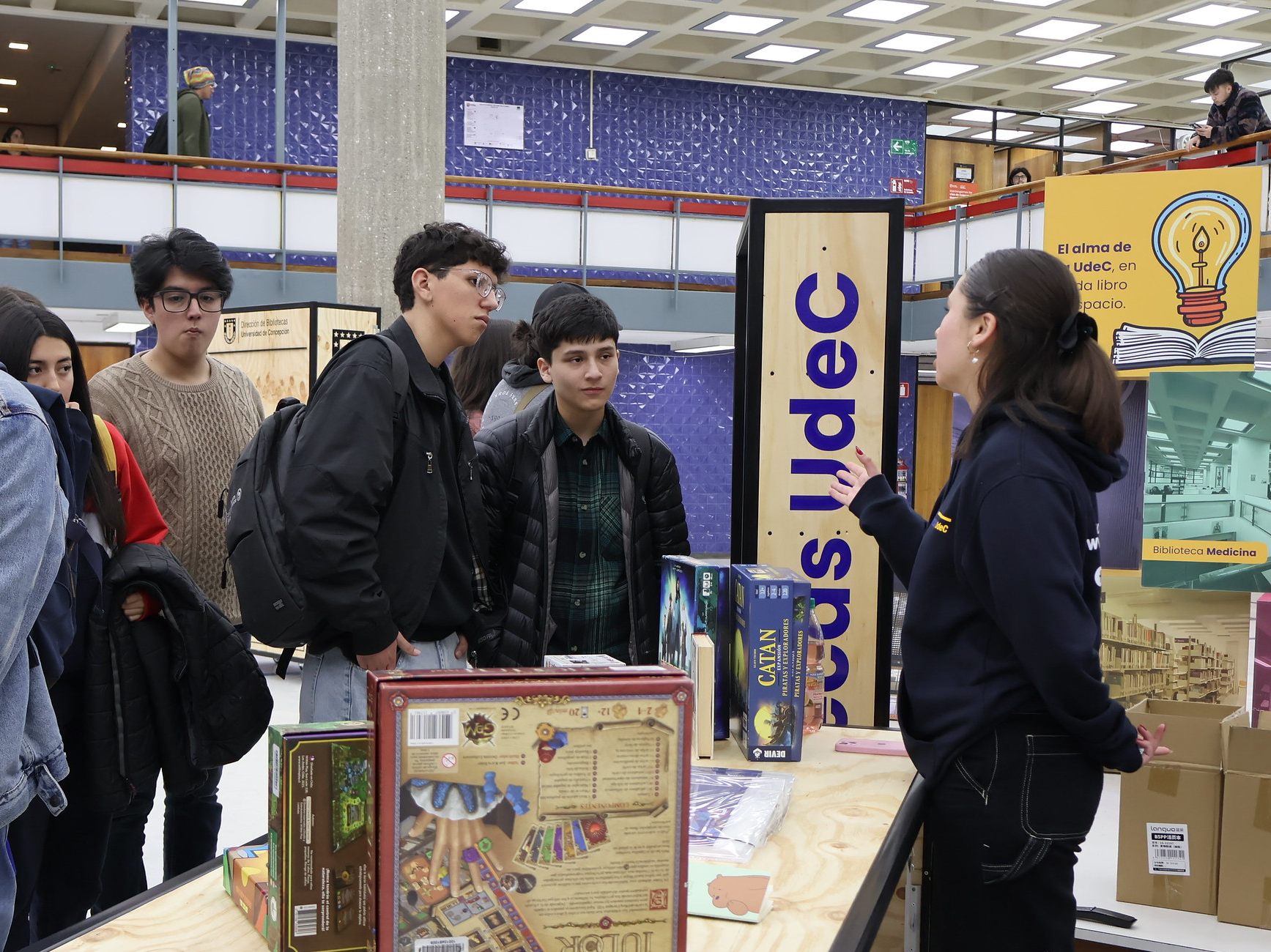 imagen que muestra a monitora conversando con asistentes a feria en hall de Biblioteca Central