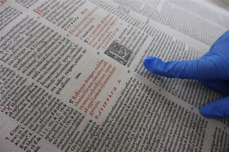 Persona con guante de protección revisa incunable que resguarda la Universidad de Concepción.