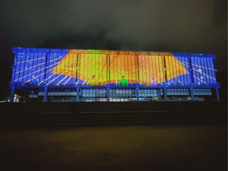 Una serie de figuras son proyectadas en la fachada de la Biblioteca Central UdeC durante videomapping