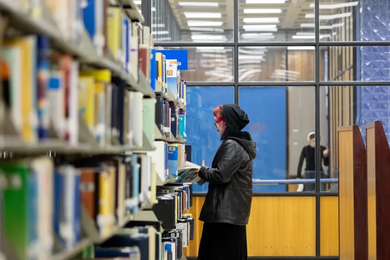 Estudiante revisa libro en estantería del tercer piso de Biblioteca Central UdeC