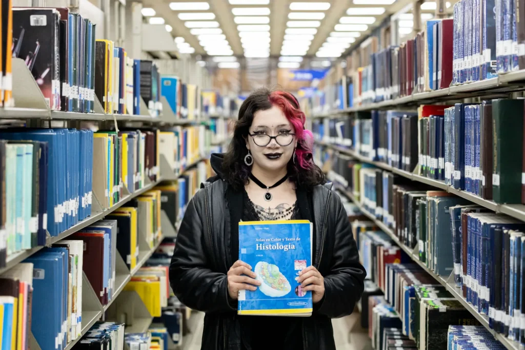 Estudiante muestra libro seleccionado en estanterías de la Biblioteca Central